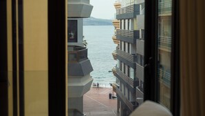 Blick aus einem Fenster auf ein Gewässer mit modernen Gebäuden im Hintergrund.