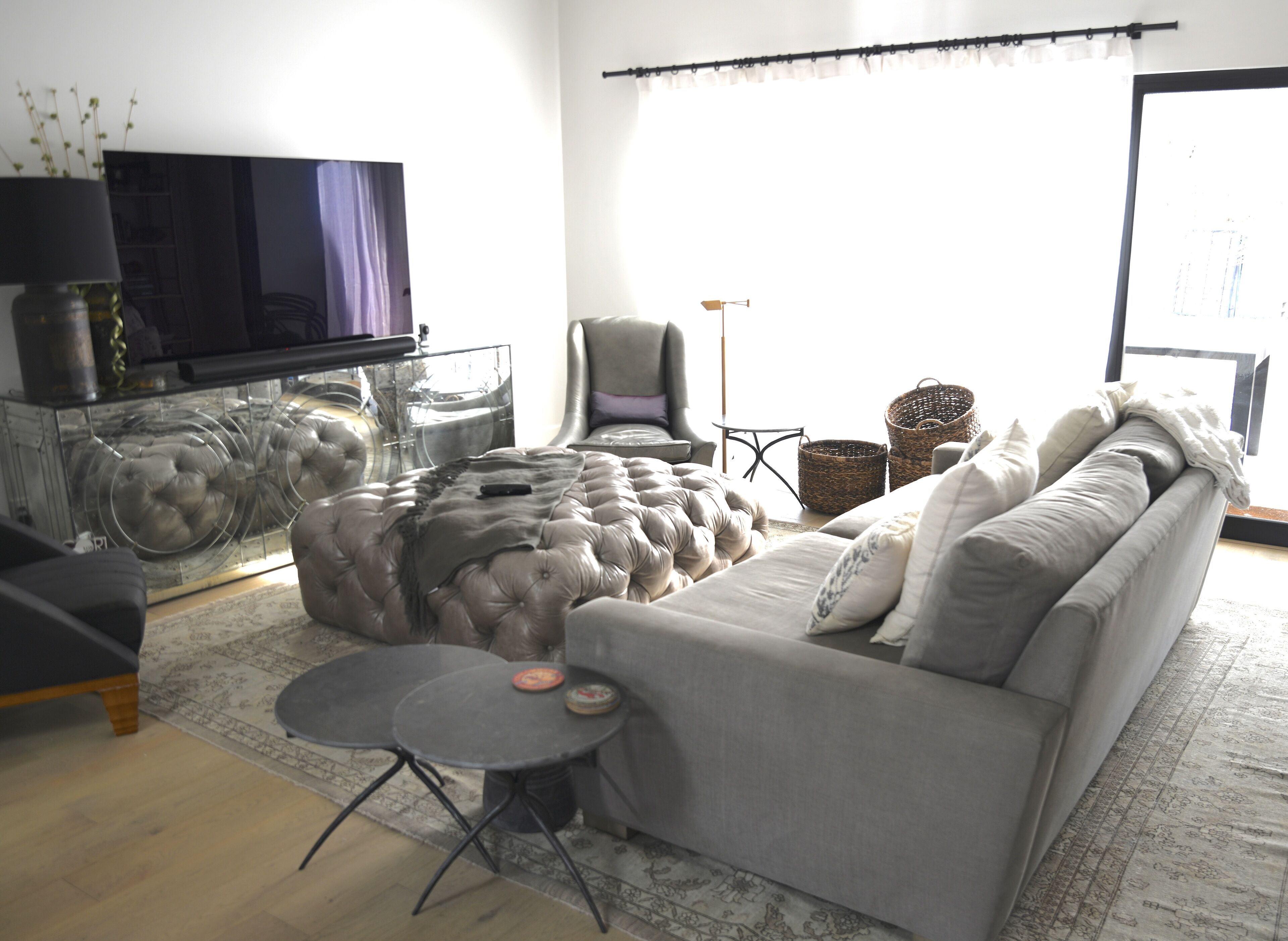 A modern living room with a grey sofa, a glass coffee table, and a television on a stand.