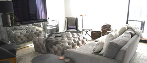 A modern living room with a grey sofa, a glass coffee table, and a television on a stand.