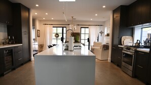 A modern kitchen with dark cabinetry, a central island, and a dining area with a white chair.