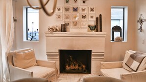 A living room with a fireplace, two armchairs, a chandelier, and butterfly wall art.