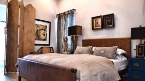 A bedroom with a wooden bed, a nightstand, a lamp, and a curtain.