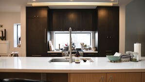 A modern kitchen with dark wooden cabinets, a large island with a sink, and a view of the outdoors through a window.