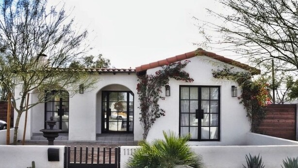 A single-story house with a white exterior, a red-tiled roof, and a small front garden with cacti and a palm plant.