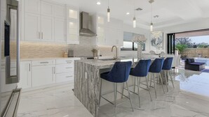 Una cocina moderna con gabinetes blancos, una isla de mármol y taburetes de bar.