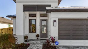 Una casa moderna de dos pisos con garaje, puerta principal y un pequeño jardín delantero con plantas.