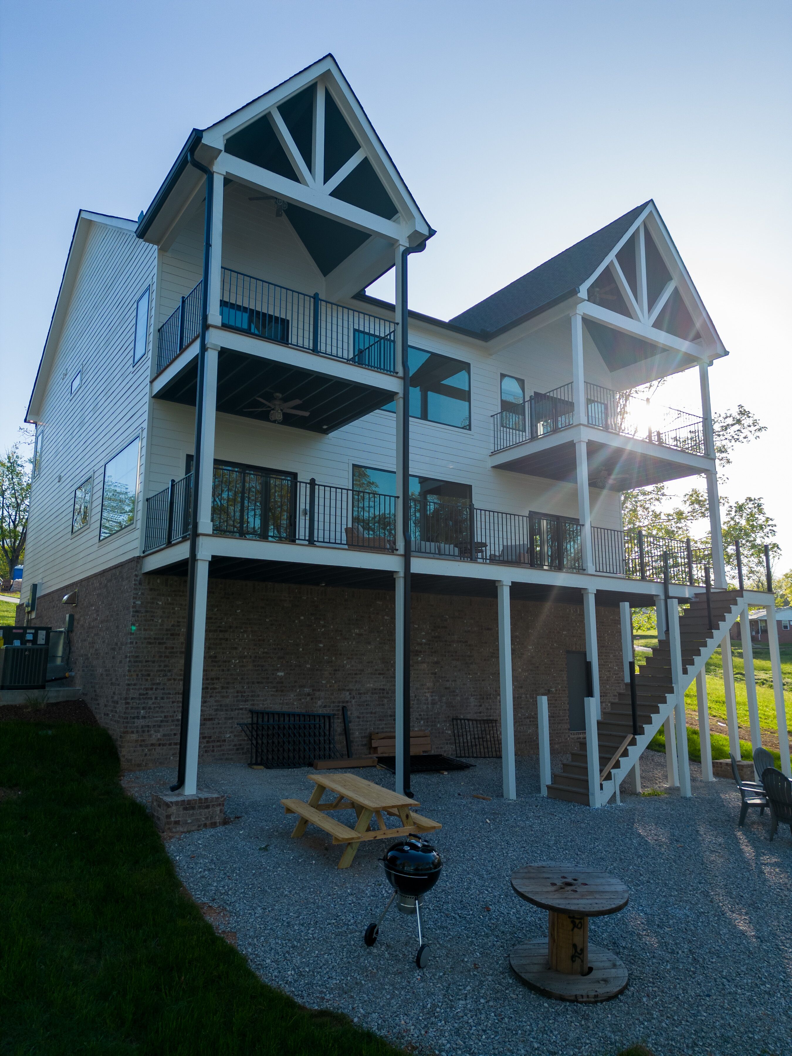 A two-story building with a balcony on the upper floor, a wooden picnic table, and a barbecue grill in the foreground.