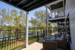 A covered outdoor deck with wicker furniture, a view of a lake, and a second-story balcony with a railing.