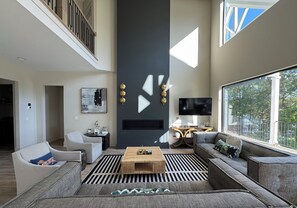 A modern living room with a flat-screen TV, a large window, and a staircase.