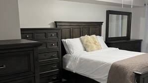 A bedroom with a dark wood bed, white bedding, a fluffy pillow, a dresser, and a ceiling fan. - 5 Mins from Nordic Spa Whitby (Whitby)