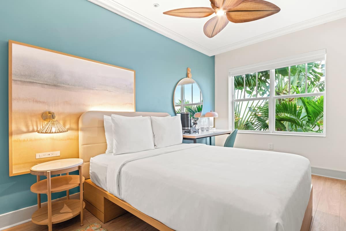 Une chambre moderne avec un grand lit, une table de chevet, un miroir et une fenêtre donnant sur un paysage verdoyant.