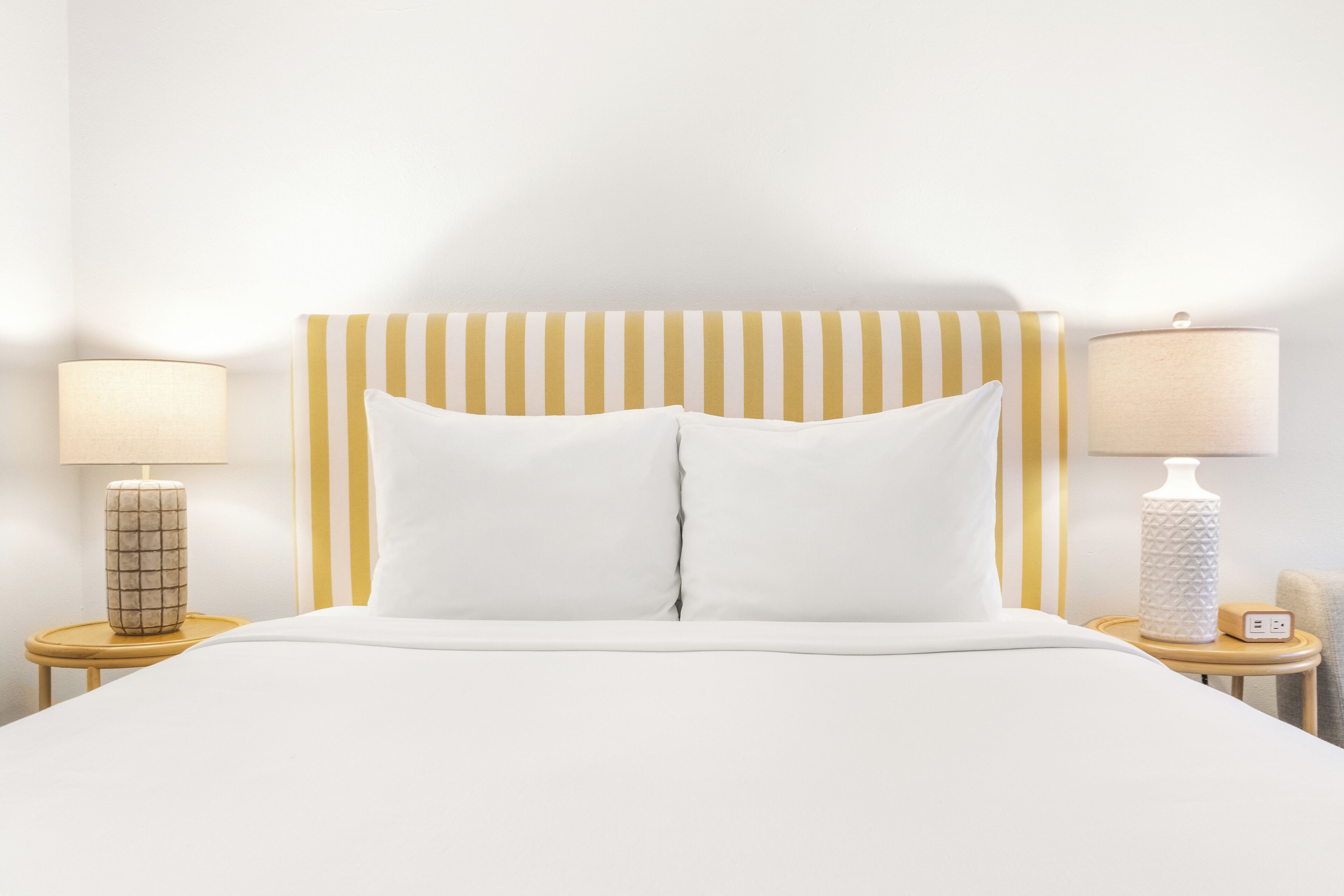 Ein ordentlich bezogenes Bett mit einem gestreiften Kopfteil, zwei Nachttischlampen und einem kleinen Tisch mit einer Lampe.