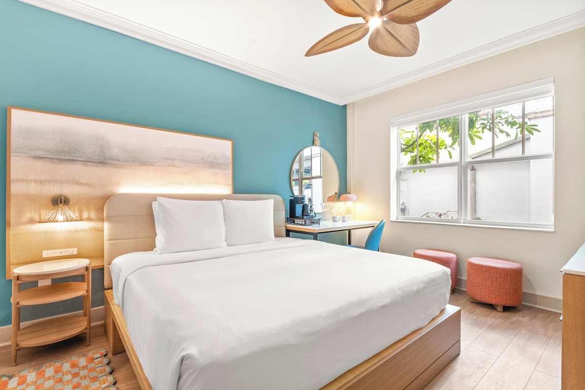 Une chambre à coucher comprenant un lit, une table de chevet, une lampe, un miroir, une fenêtre et un ventilateur de plafond.