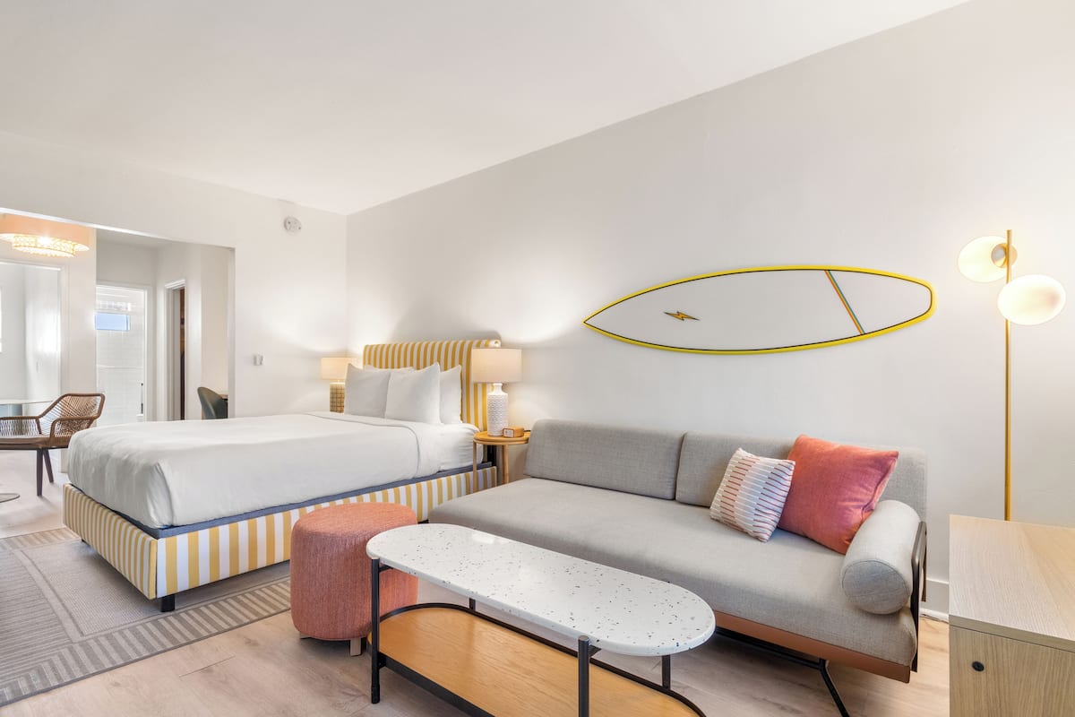 Une chambre d’hôtel avec un lit, un canapé, une petite table, une lampe et un miroir ovale fixé au mur.