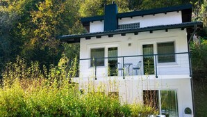 Une maison à deux étages dotée d’un balcon, entourée d’une forêt dense.