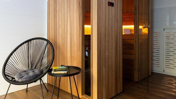 Un intérieur en bois avec une chaise noire et une petite table, une porte en bois avec une poignée, et un luminaire fixé au mur.