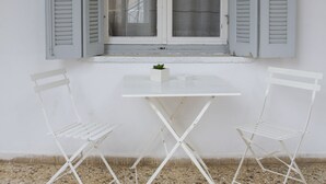 Een witte tafel met twee witte stoelen voor een raam met grijze luiken.