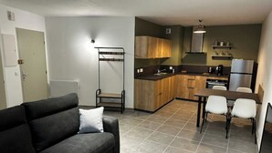 A compact living space with a sofa, a dining table with chairs, a kitchenette, and a bunk bed.