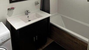 A modern bathroom with a white sink, dark cabinets, a large mirror, and a shower area.