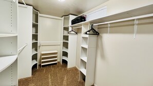 Armadio a muro con scaffalature bianche, pavimento rivestito di moquette e una luce a soffitto.