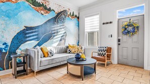 Una sala de estar con un mural grande, un sofá gris, una mesa de centro y una puerta decorada con un adorno.