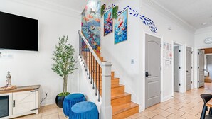 Una escalera con barandilla de madera, un televisor de pantalla plana montado arriba y una pared decorada con obras de arte coloridas.