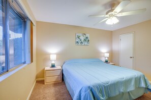 Cozy retreat with a single bed, nightstand, and ceiling fan, featuring a window and a painting of palm trees.
