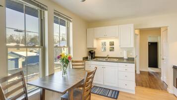 A modern kitchen with white cabinets, a wooden dining table, and a large window offering a view of the outside.