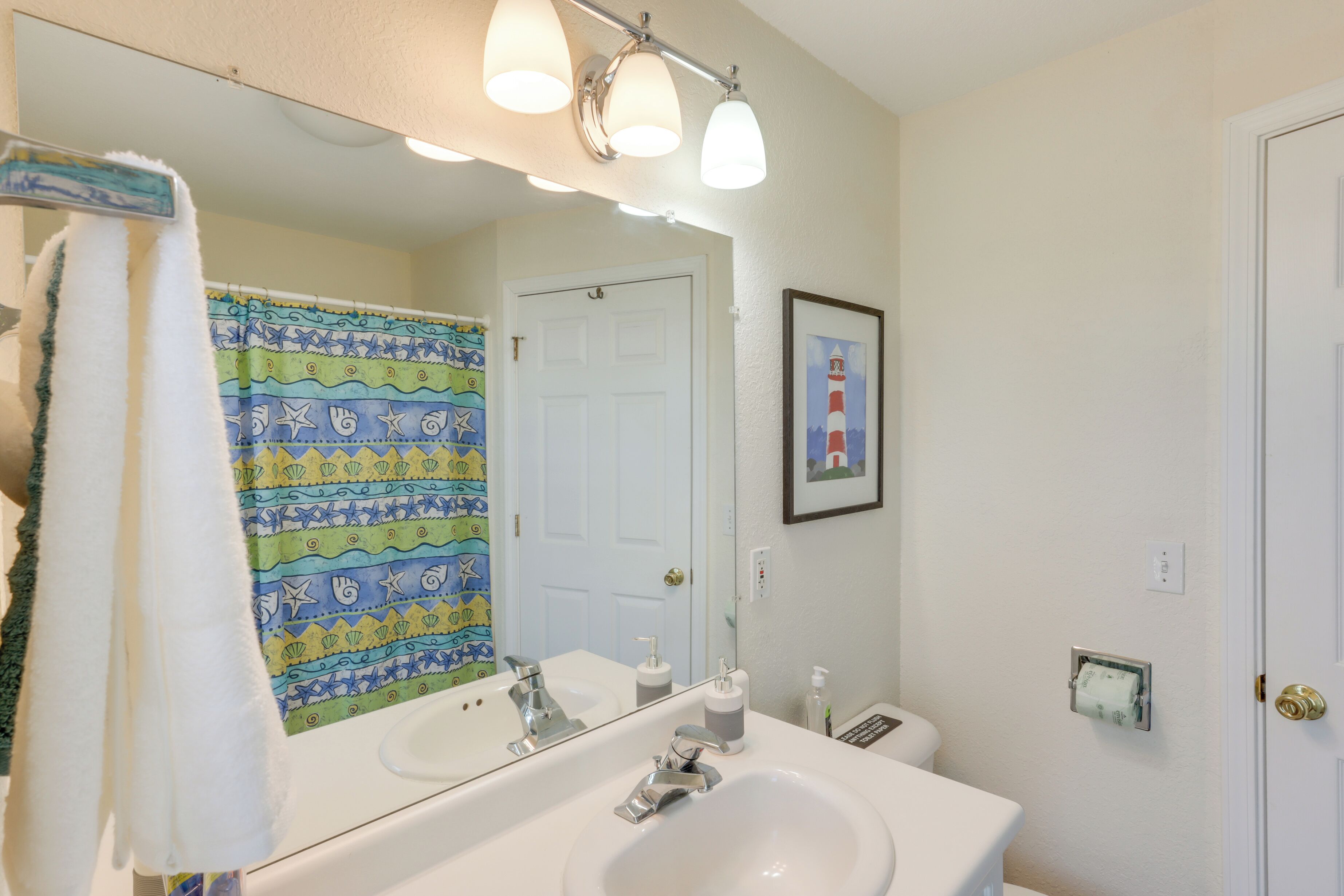 Un baño con un lavabo blanco, un espejo grande y una cortina de ducha con un estampado colorido.