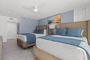 Ein Hotelzimmer mit zwei Betten, einem Deckenventilator, einem Gemälde und einem Fenster mit Jalousien.