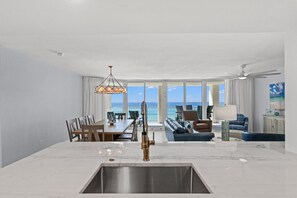 Ein modernes Interieur mit Kücheninsel, Essbereich und Sitzgelegenheit an einem großen Fenster mit Meerblick.