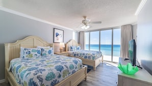 A bedroom with two beds, a ceiling fan, a TV, and a view of the ocean. - Edie's Escape-Long Beach 501T3-3BD/3BTH End Unit-2 Sets of Beach Chairs Included! (Panama City Beach)