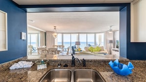 A kitchen with a double sink, granite countertop, and a view of the living area with a balcony overlooking the ocean. - Edie's Escape-Long Beach 501T3-3BD/3BTH End Unit-2 Sets of Beach Chairs Included! (Panama City Beach)