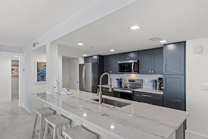 A modern kitchen with a marble countertop, stainless steel appliances, and a bar area with stools.