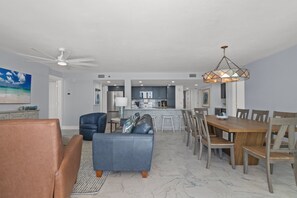 A modern living room with a sofa, chairs, and a dining table. There is a kitchen area with cabinets and appliances in the background. - Edie's Escape-Long Beach 501T3-3BD/3BTH End Unit-2 Sets of Beach Chairs Included! (Panama City Beach)