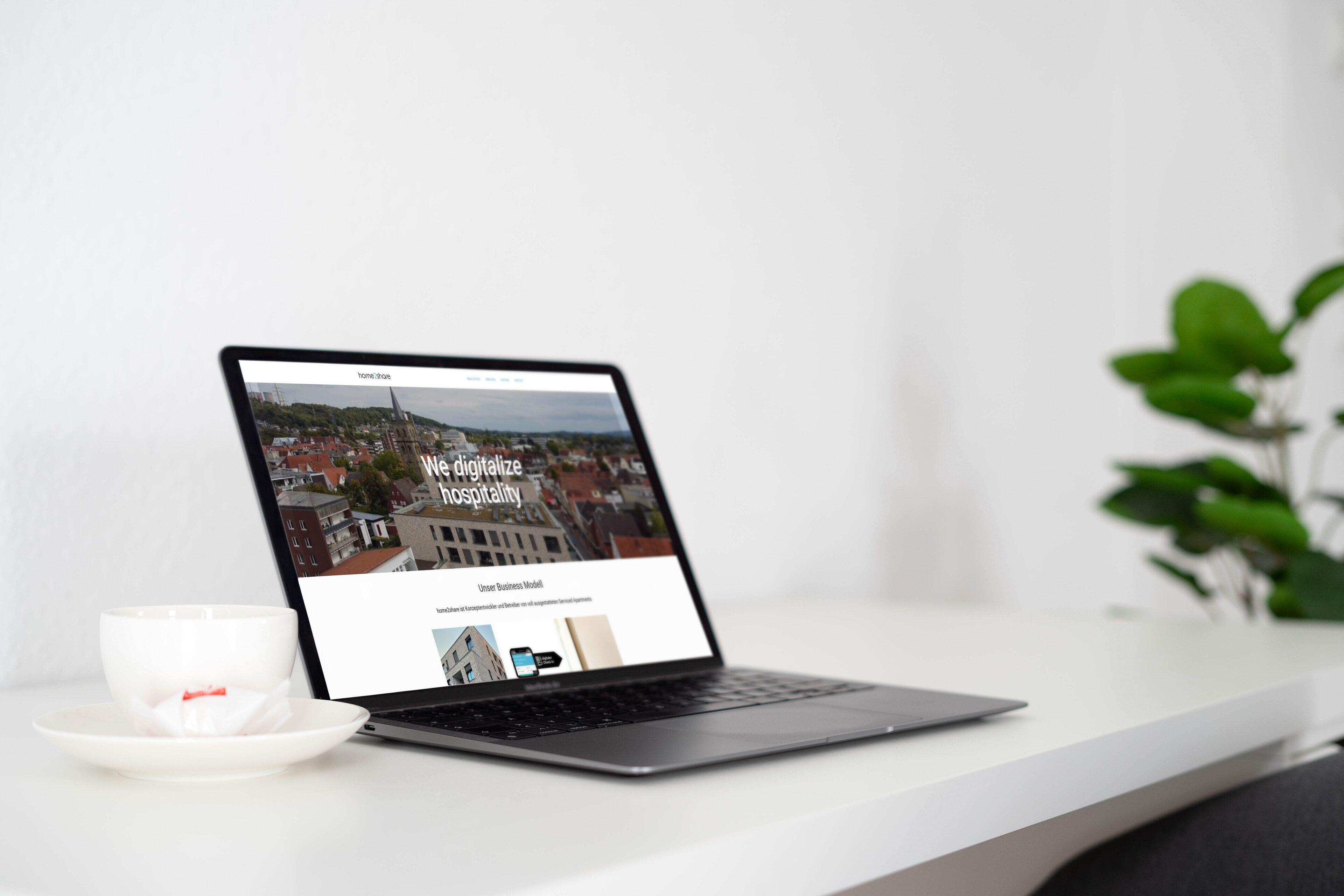 A laptop on a white table displaying a webpage with the title "We digitalize hospitality" and a subtitle "Unser Business Modell".