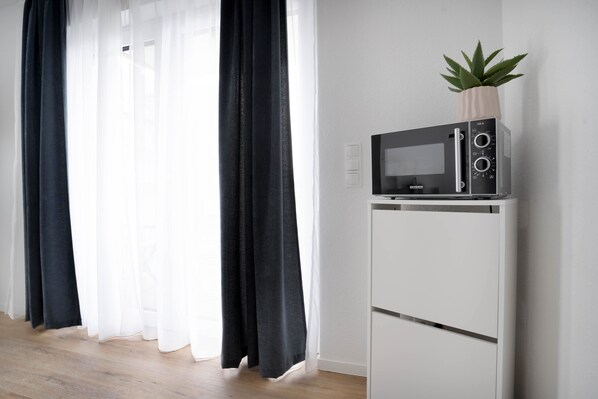 A modern kitchen with a microwave on a white stand, a potted plant, and sheer curtains.
