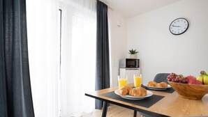 A modern dining area with a table set for breakfast, including croissants, fruit, and juice. A microwave and a clock are visible on the wall. - Deluxe apartment in the centre of OS (Osnabrueck)