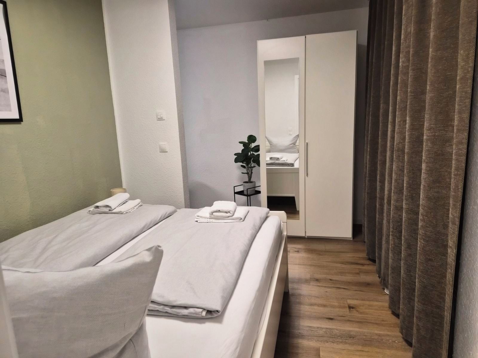 Hotellihuone, jossa on kaksi sänkyä, yöpöytä, jossa on kasvi, vaatekaappi ja verho.