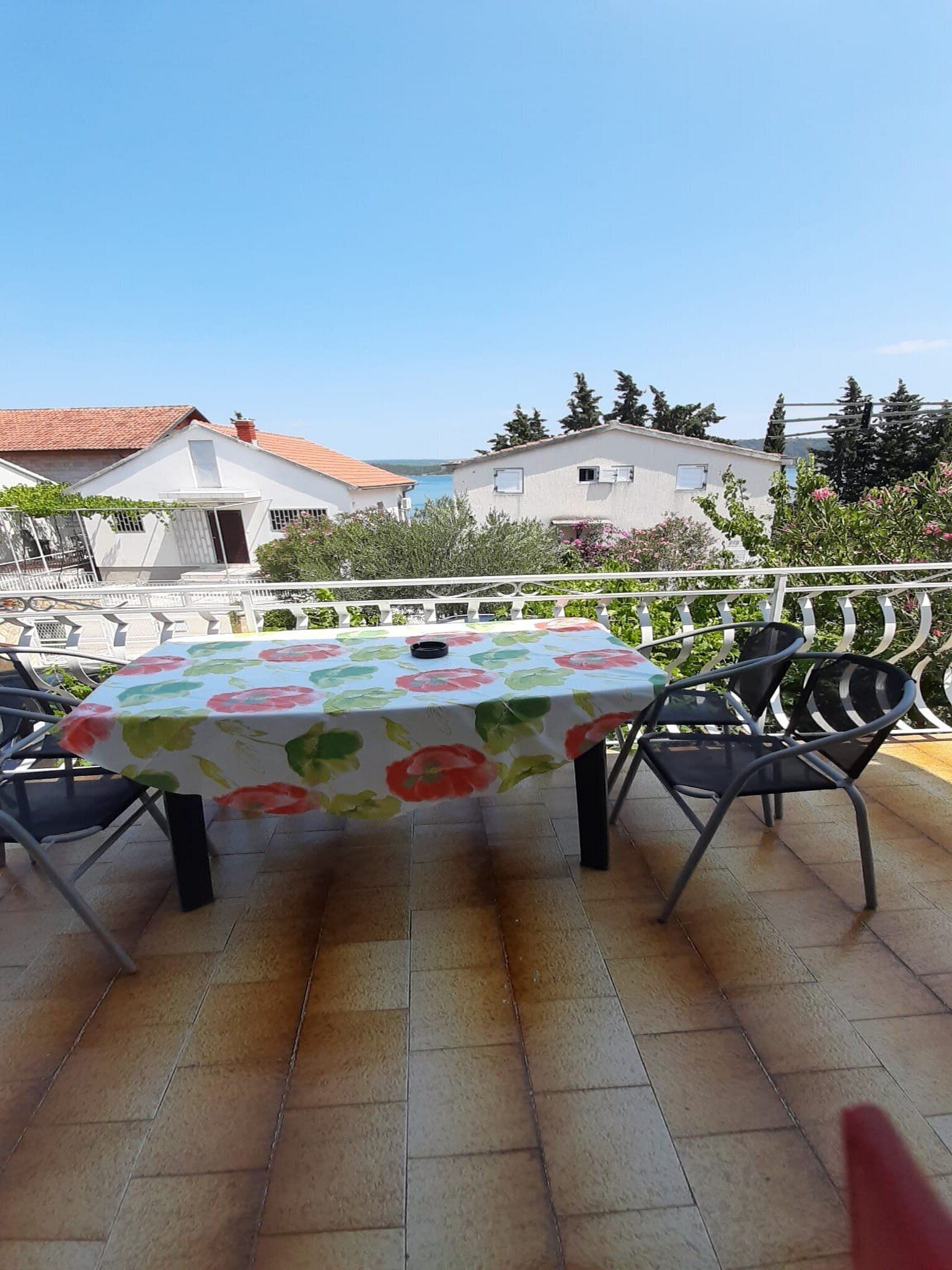 An outdoor patio with a table covered in a floral tablecloth, surrounded by metal chairs.