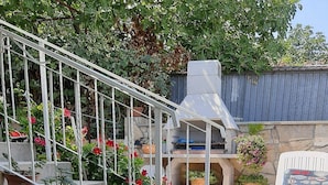 A patio area with steps leading to a barbecue grill, surrounded by potted plants and a white chair. - Apartment by the Beach (Bilice)
