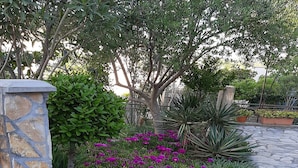 A stone pathway with a stone wall on one side and a garden with purple flowers and green foliage. - Apartment by the Beach (Bilice)