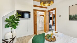 Une chambre à coucher moderne, avec un lit, une télévision, une plante et une porte en bois donnant sur une salle de bain.