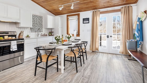 Une cuisine moderne avec des meubles blancs, un plafond en bois et un coin repas avec une table dressée pour quatre personnes.