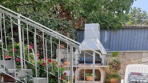 Un espace patio agrémenté d’un escalier en pierre, de plantes en pot, d’un barbecue et d’une chaise blanche.