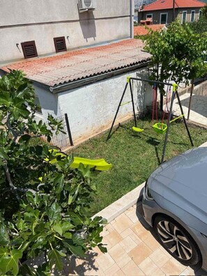 Uma área residencial com um edifício branco, telhado de telhas vermelhas, um balanço e um carro estacionado.