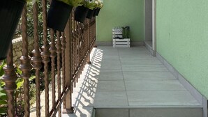 Un balcón con pared verde, baranda de madera y plantas en macetas.