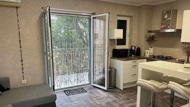 Un espacio habitable compacto con kitchenette, un sofá, zona de comedor y puerta corrediza de cristal que da a un balcón.