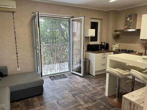 A compact living space with a kitchenette, a sofa, a dining area, and a sliding glass door leading to a balcony.