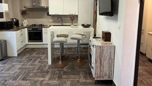 Una cocina moderna con armarios blancos, una isla central con taburetes de bar, horno empotrado y un televisor de pantalla plana montado en la pared.